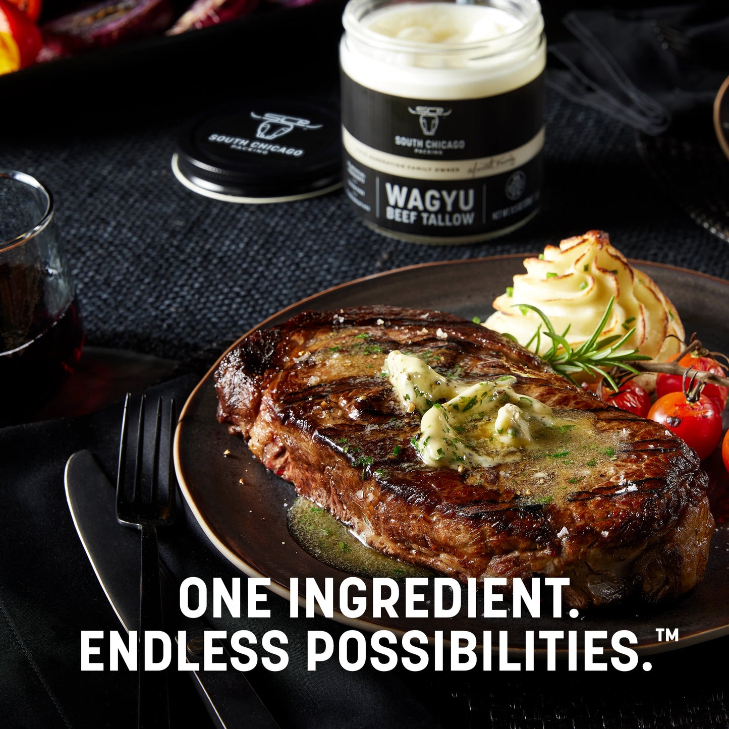 Steak with butter on a plate, accompanied by a container of Wagyu beef tallow, on a dark surface.