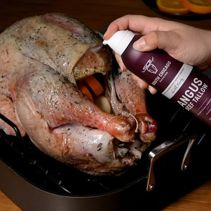 A hand holding a bottle of South Chicago Creamery Angus Beef Tallow rub against a roasted turkey in a black roasting pan.