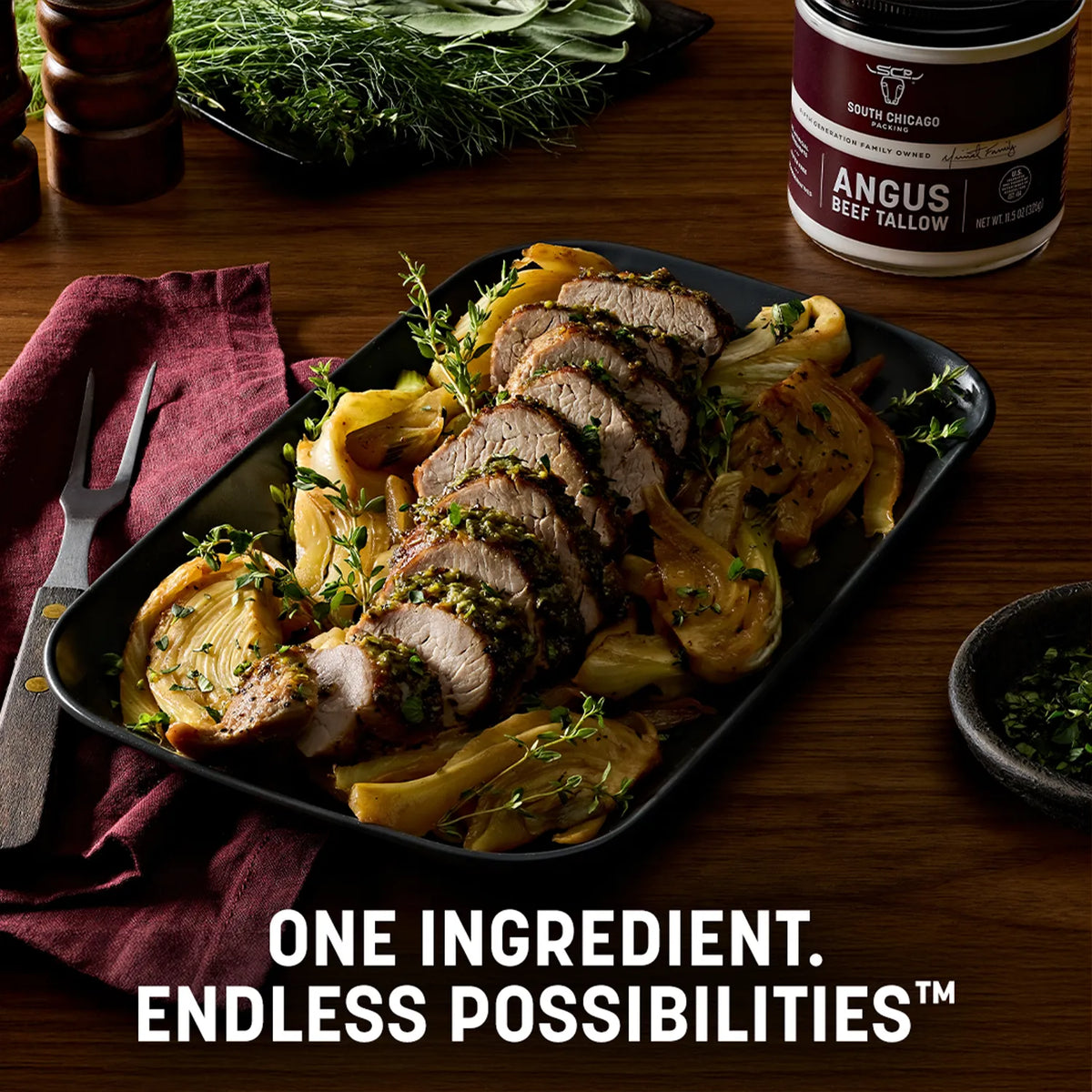 Sliced cooked beef tenderloin served on a black rectangular platter with roasted onions and herbs, set on a wooden table. A canister of South Chicago Angus Beef Tallow is visible in the background, along with a fork, napkin, and text overlay reading 'ONE INGREDIENT.