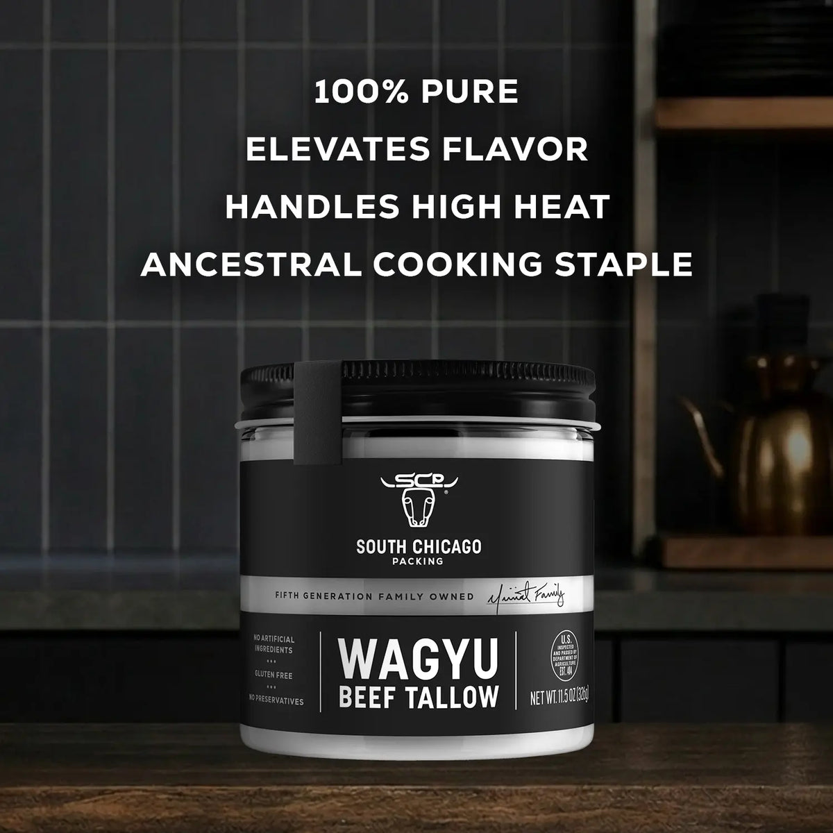 A jar of South Chicago Packing Wagyu Beef Tallow shown on a dark kitchen countertop with a tiled backsplash and a teapot in the background. White text at the top reads '100% PURE Elevates Flavor Handles High Heat Ancestral Cooking Staple'.